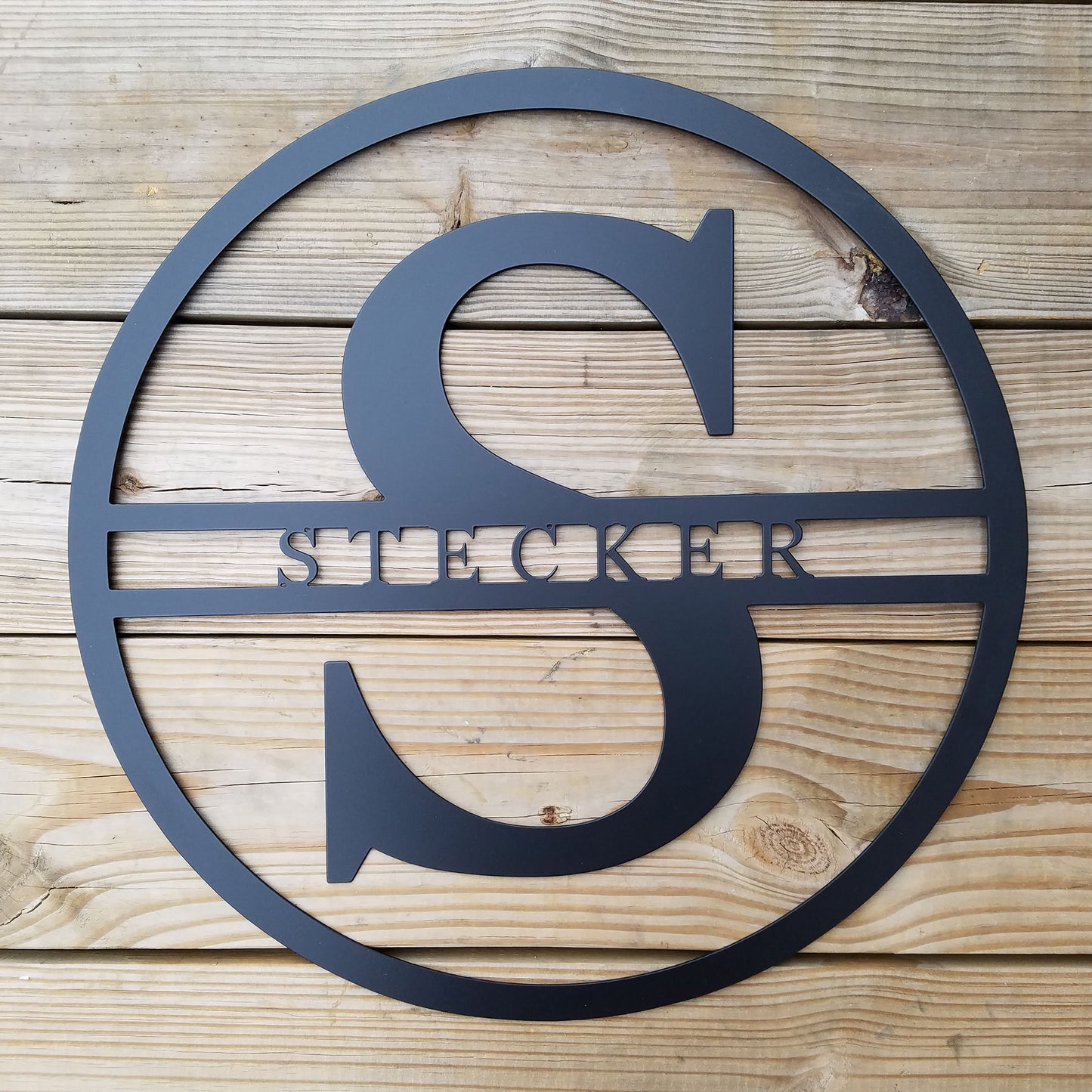 Modern Round Personalized Family Name & Initial Metal Sign with "STECKER" personalization shown on a wood plank background