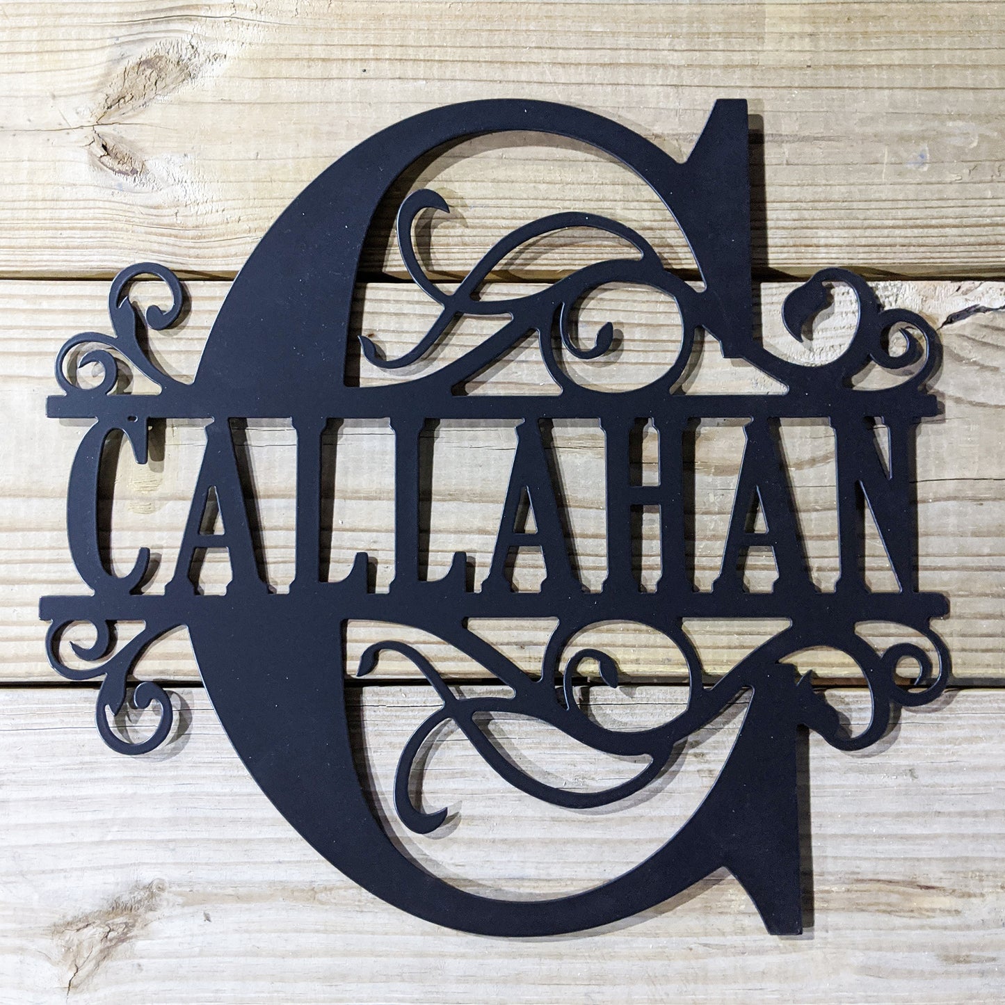 Scroll Monogram Family Name Sign with "C Callahan" personalization shown on wood plank background