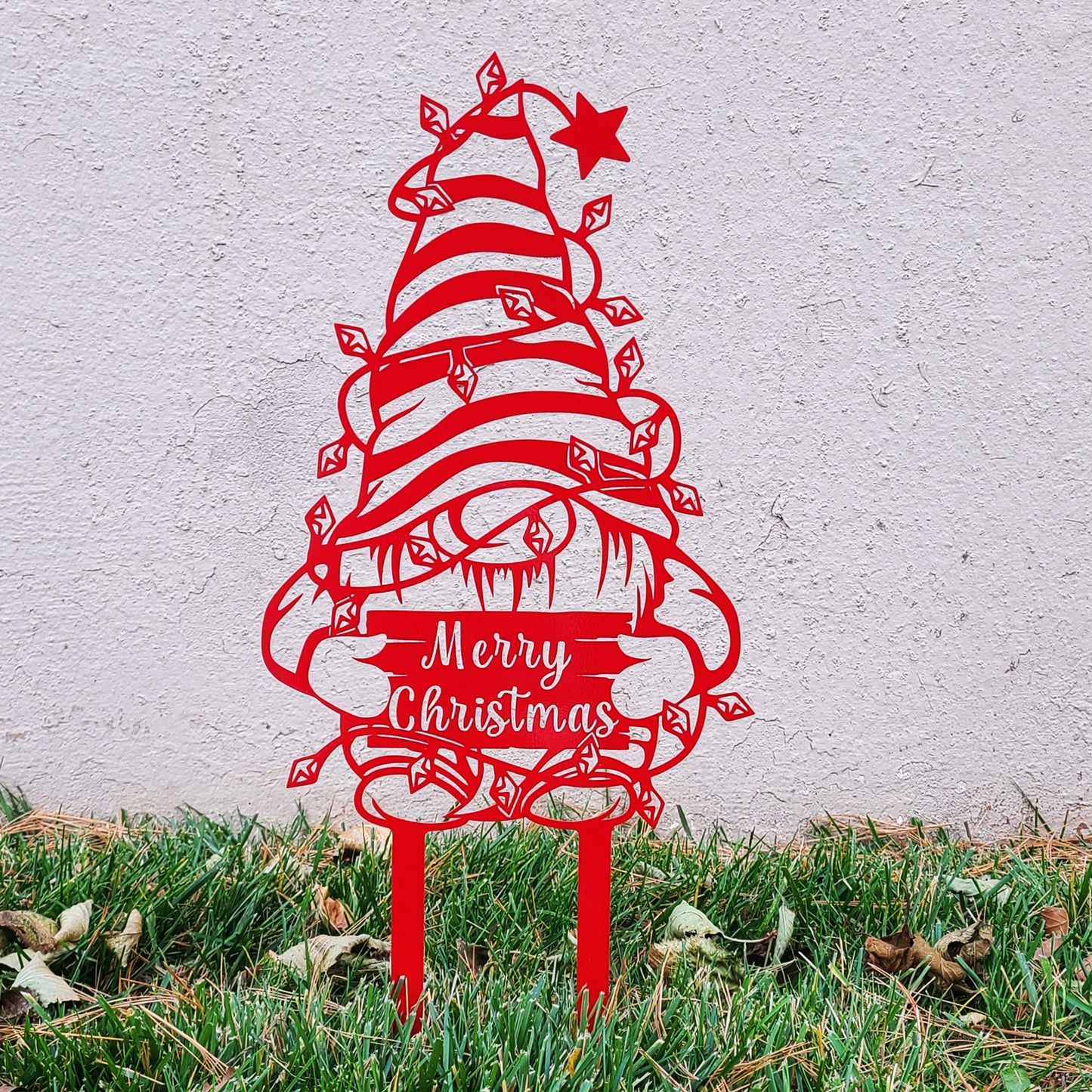 Christmas Gnome Metal Garden Sign red in grass in front of stucco wall